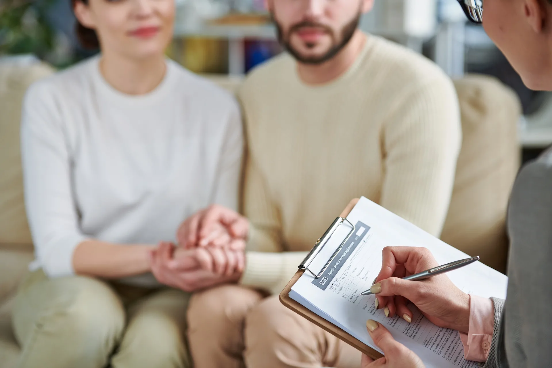 Par sidder og holder hinanden i hånden mens en kvinde notere ned på et stykke papir