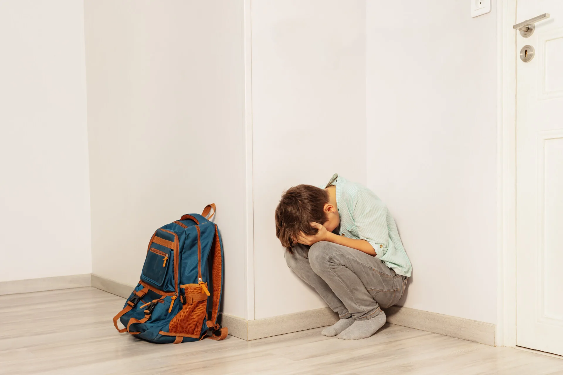 Dreng sidder med hovedet gemt i hænderne ude foran en dør