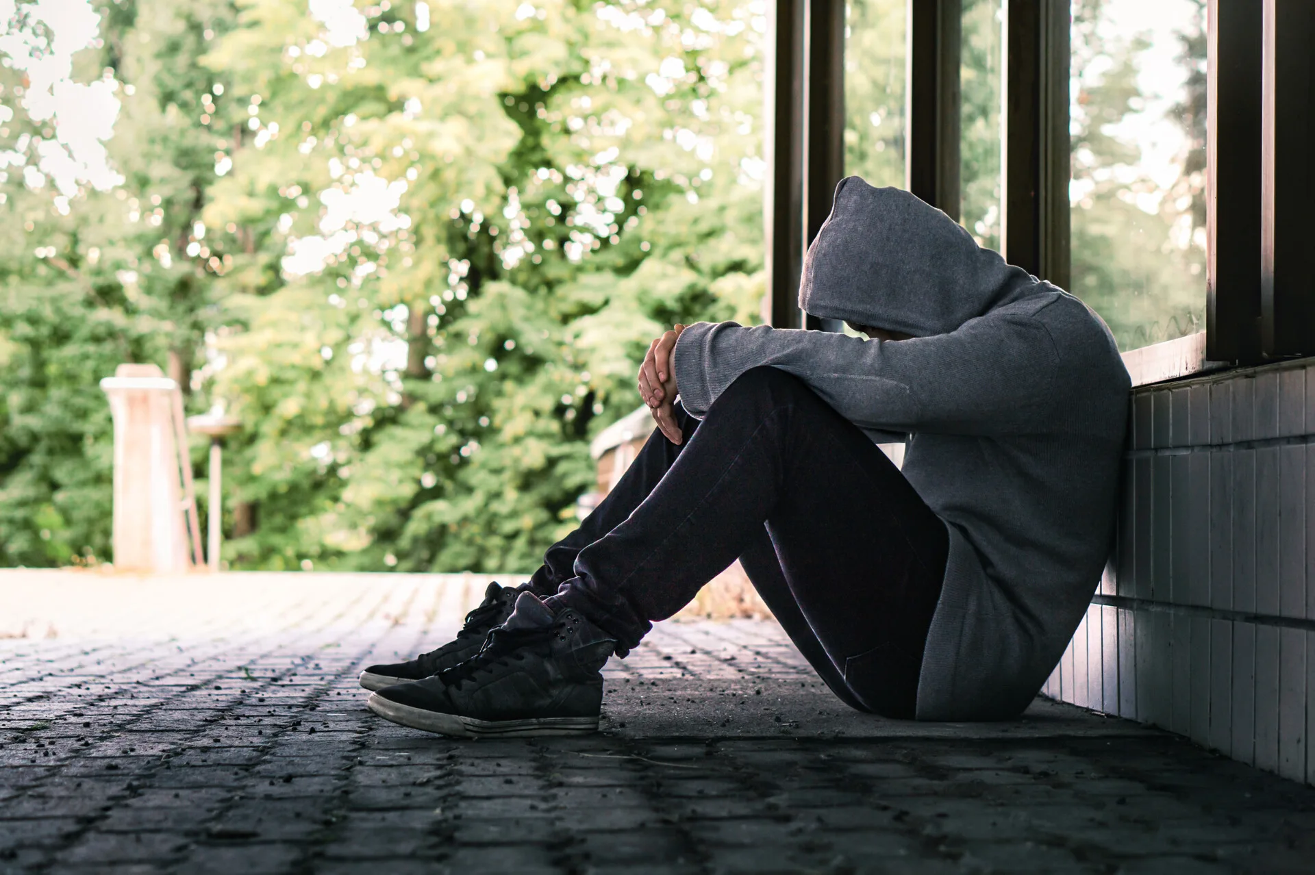 Mand sidder sammen krøllet ude foran et hus