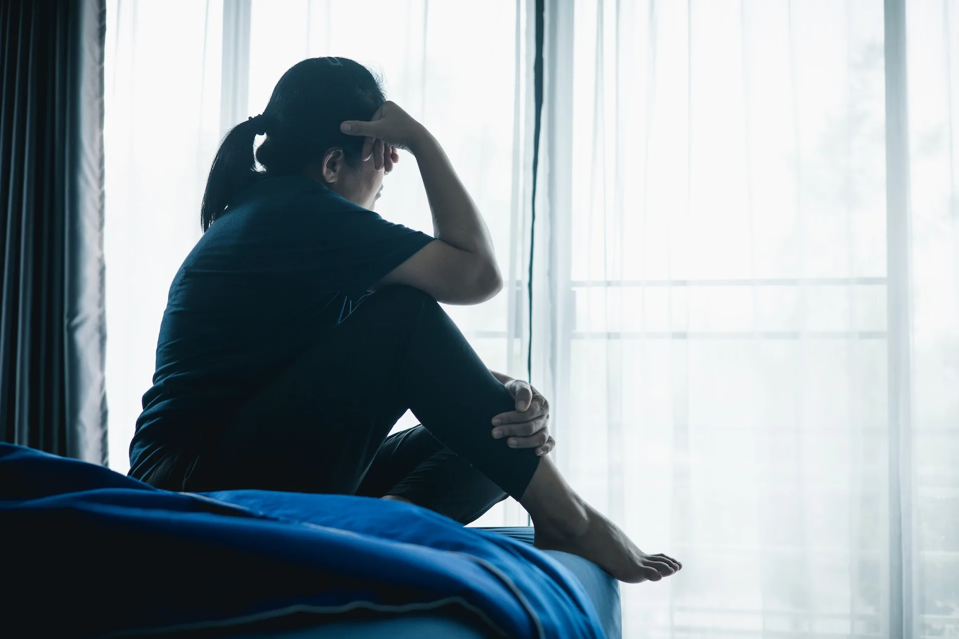 Kvinde sidder på sengen med benet trukket op under sig