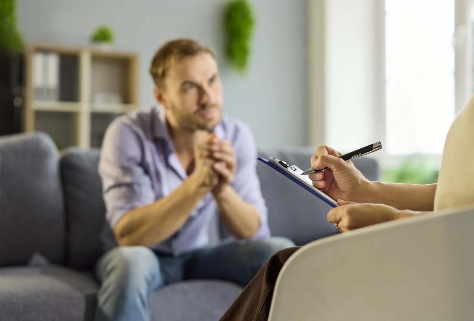 Mand sidder i sofa, mens en anden person skriver ned på en blok